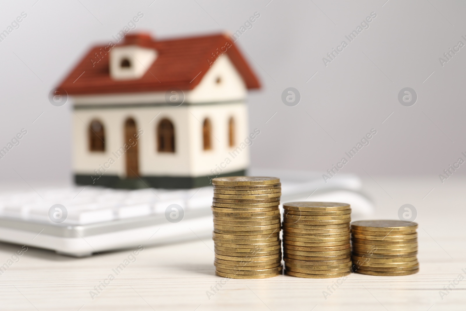 Photo of Mortgage concept. Stacks of coins, model house and calculator on white wooden table, selective focus