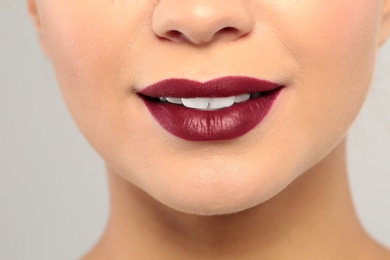 Photo of Young woman wearing dark lipstick on gray background, closeup