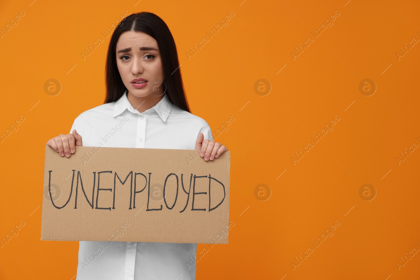 Photo of Young woman holding sign with word Unemployed on orange background, space for text