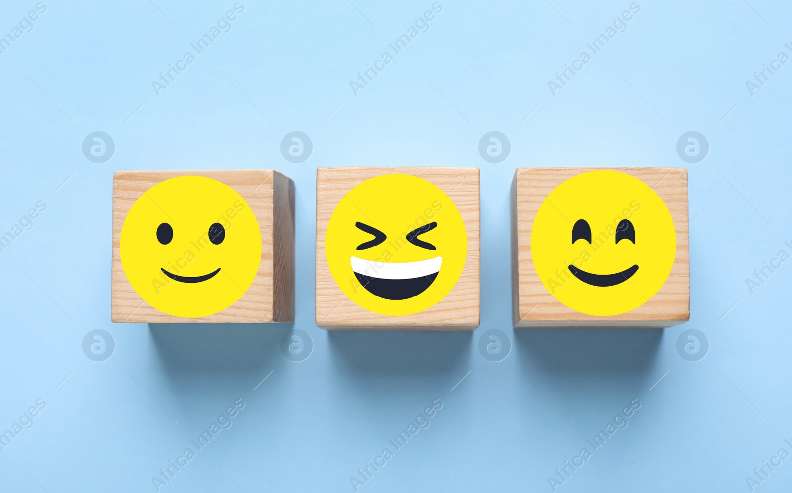 Image of Wooden cubes with different emoticons on light blue background, flat lay