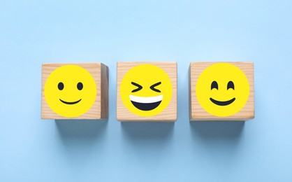 Wooden cubes with different emoticons on light blue background, flat lay