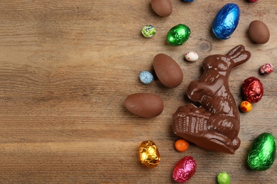 Photo of Chocolate Easter bunny and eggs on wooden table, flat lay. Space for text