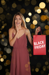Image of Black Friday sale. Happy young woman with shopping bag on dark background, bokeh effect