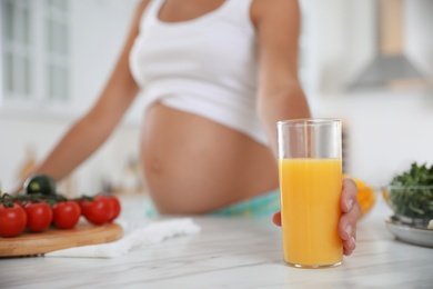 Photo of Young pregnant woman with glass of juice at table in kitchen, closeup. Taking care of baby health