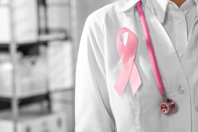 Photo of Doctor with stethoscope and pink ribbon indoors, closeup and space for text. Breast cancer awareness