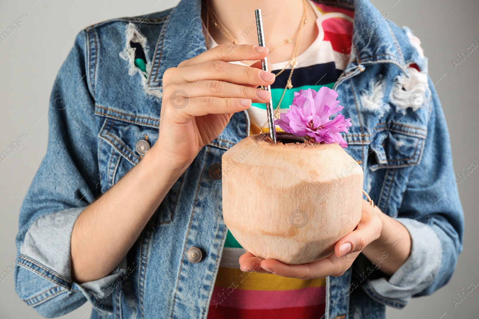 Photo of Woman holding fresh young coconut with straw on grey background, closeup