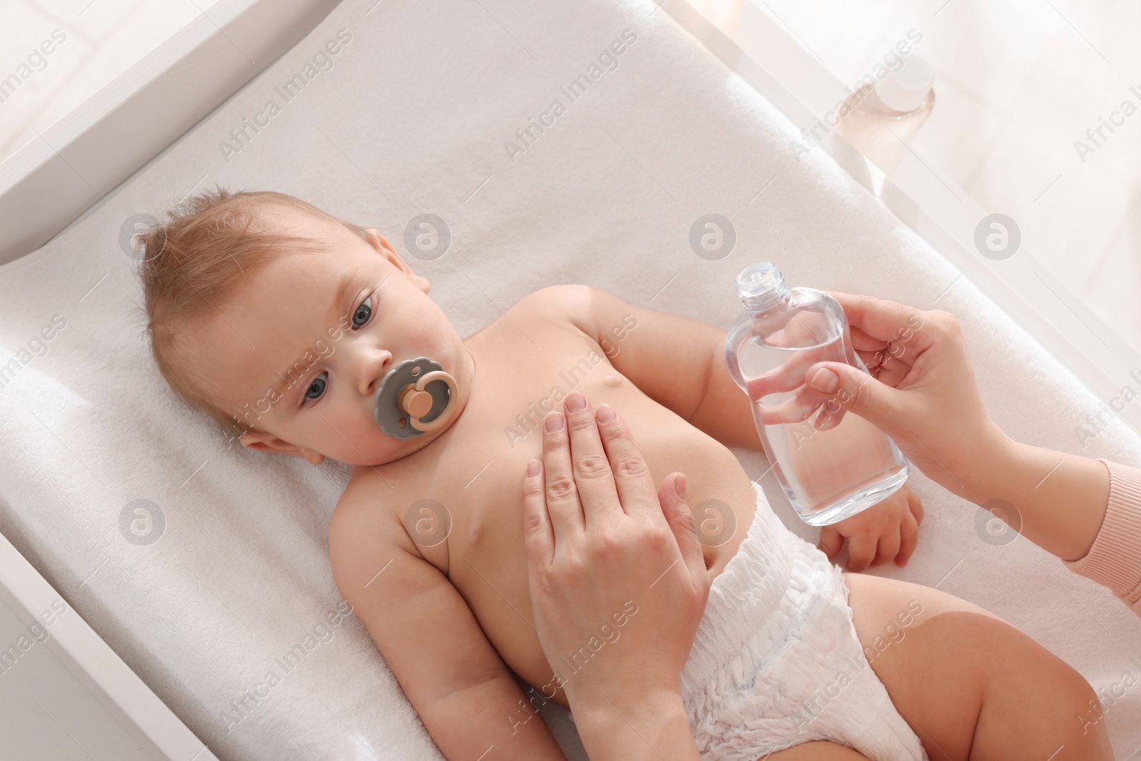 Photo of Mother massaging her cute baby with oil on changing table, above view