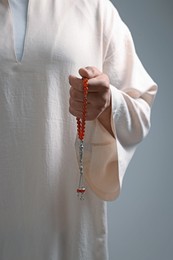 Photo of Muslim man with misbaha on light grey background, closeup
