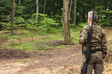 Photo of Man with hunting rifle wearing camouflage in forest, back view. Space for text