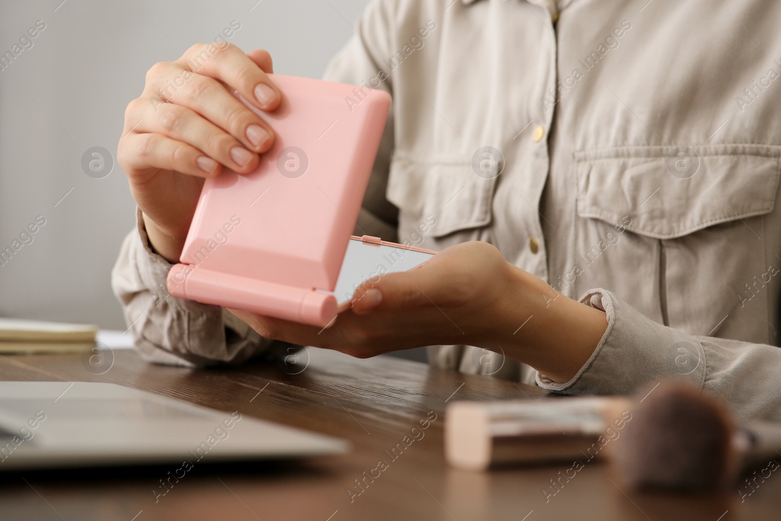 Photo of Woman with cosmetic pocket mirror at wooden table indoors, closeup