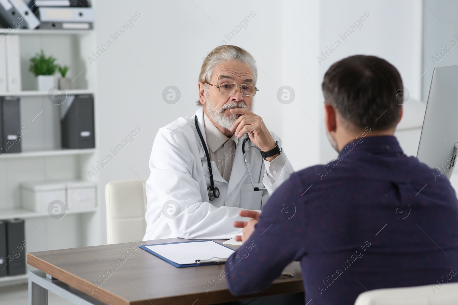 Photo of Senior doctor consulting patient at wooden table in clinic