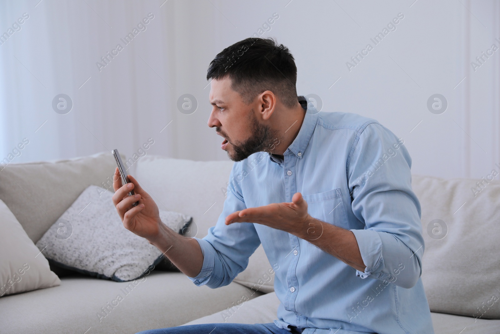 Photo of Emotional man with smartphone at home. Online hate concept