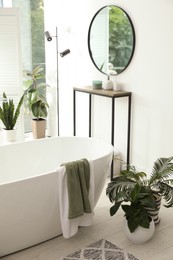 Stylish bathroom interior with modern tub, console table and beautiful houseplants. Home design