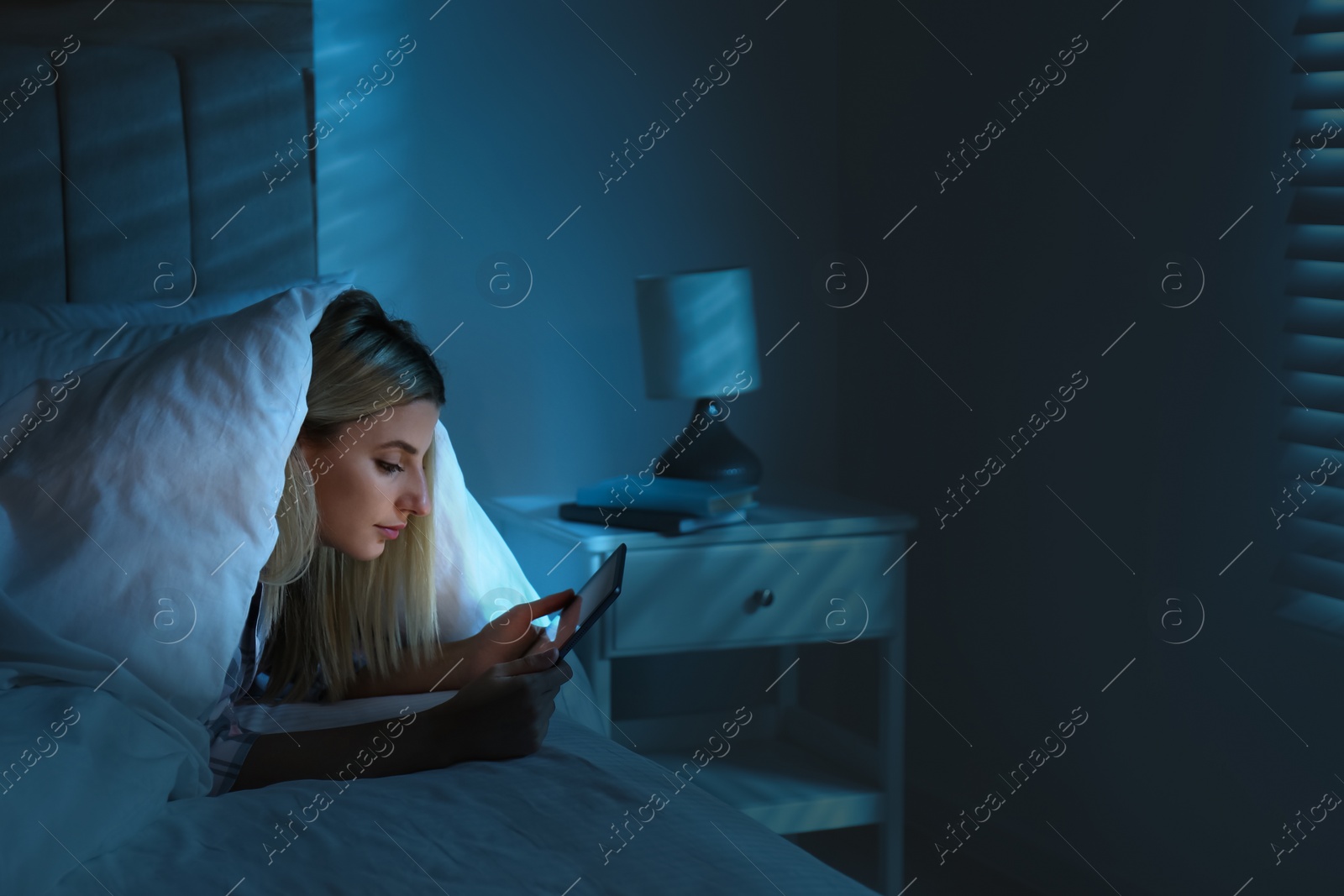 Photo of Young woman using tablet in bed at night. Sleeping disorder problem