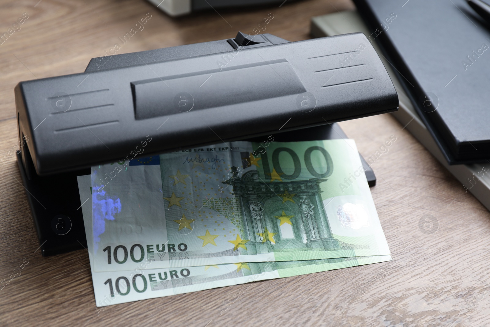 Photo of Modern currency detector with Euro banknotes on wooden table. Money examination device