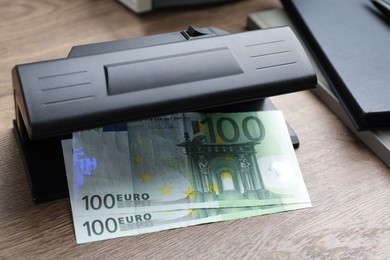 Photo of Modern currency detector with Euro banknotes on wooden table. Money examination device