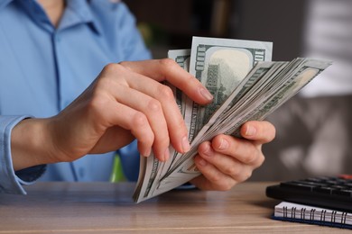 Photo of Money exchange. Woman counting dollar banknotes at wooden table, closeup