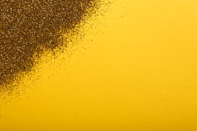 Photo of Shiny golden glitter on yellow background, top view. Space for text