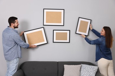 Man and woman hanging picture frames on gray wall at home