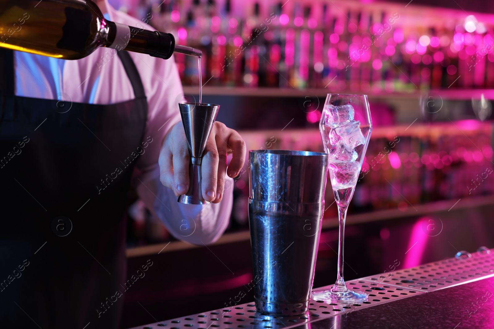 Photo of Cocktail making. Bartender pouring alcohol from bottle into jigger at counter in bar, closeup