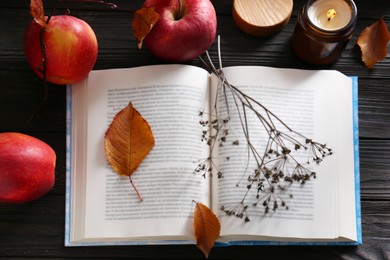 Photo of Book with dried flower, leaves as bookmark, ripe apples and candle on wooden table, above view