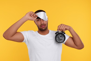 Tired man with sleep mask and alarm clock on orange background. Insomnia problem