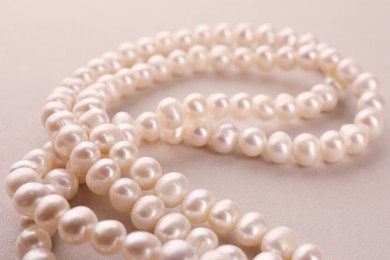 Photo of Elegant pearl necklace on beige background, closeup
