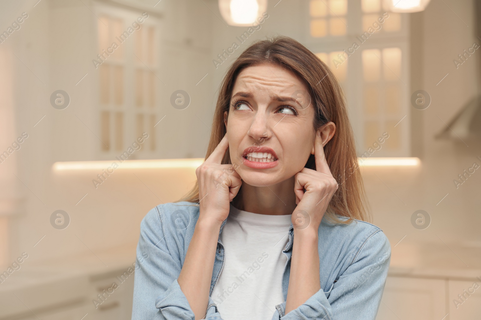 Photo of Emotional young woman covering her ears with fingers at home