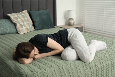 Photo of Sad young woman lying on bed at home