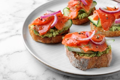 Photo of Delicious sandwiches with salmon, avocado, cucumber and onion on white marble table, closeup