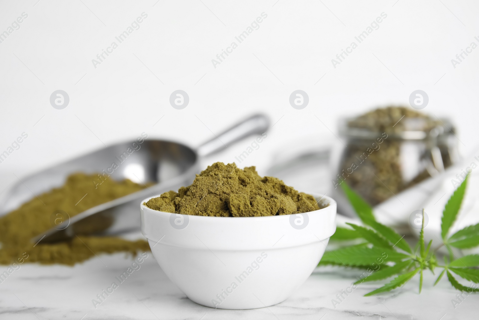 Photo of Hemp protein powder and fresh leaves on white marble table, closeup