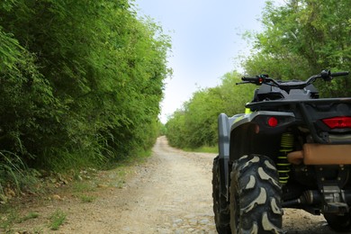 Black quad bike on pathway near trees outdoors, space for text