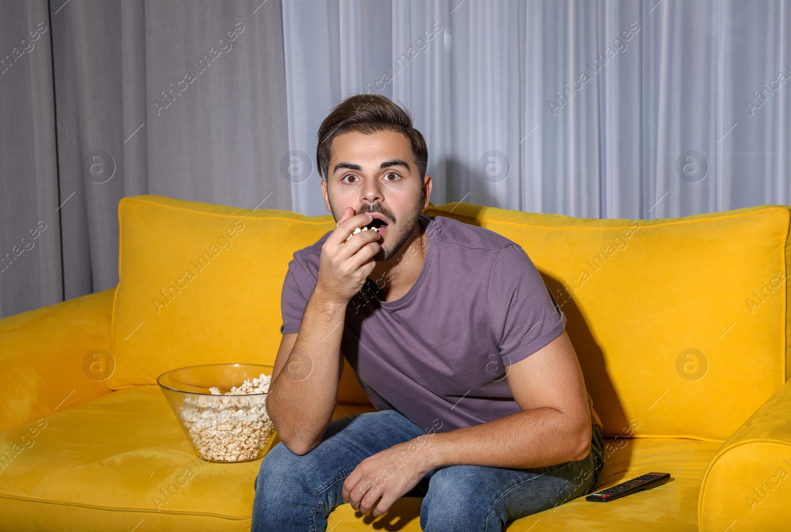 Photo of Emotional man watching with popcorn TV on couch in living room