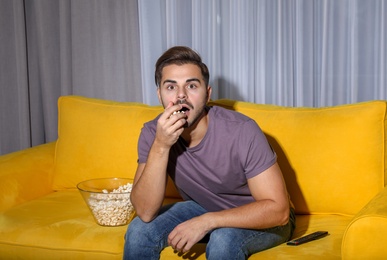 Emotional man watching with popcorn TV on couch in living room