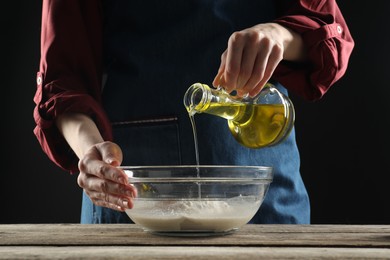 Making bread. Woman pouring oil into bowl at wooden table, closeup