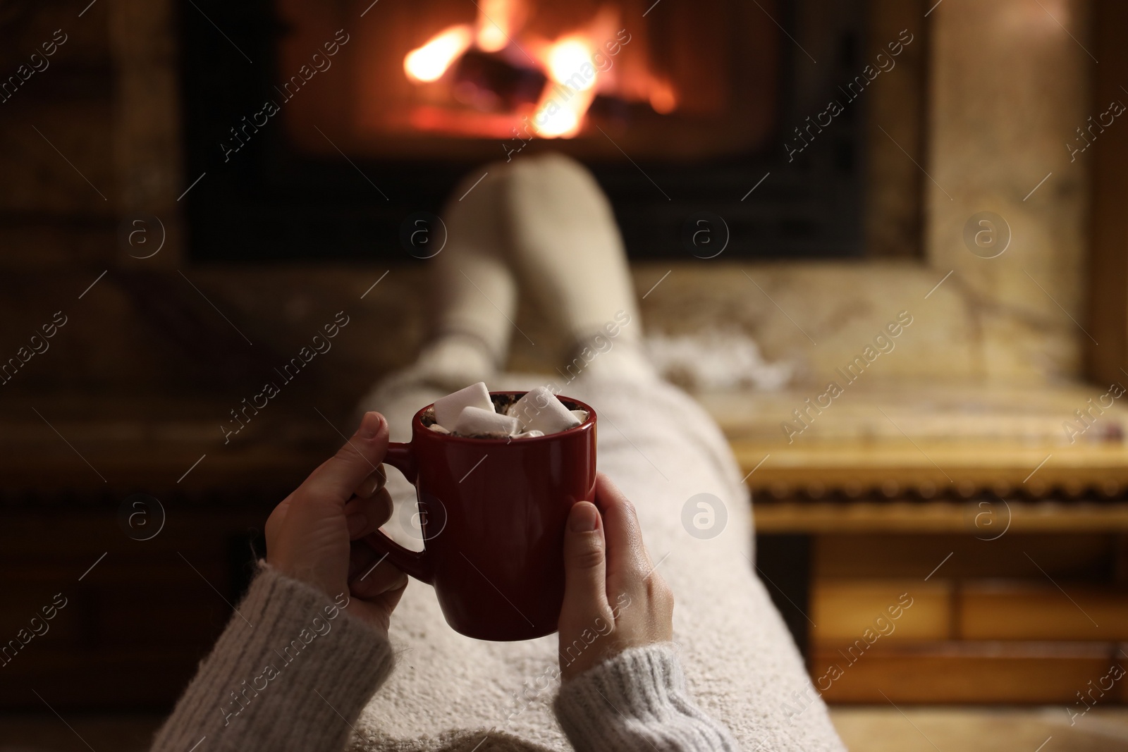 Photo of Woman with cup of hot drink resting near fireplace, closeup