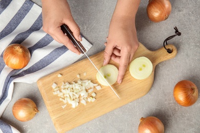 Photo of Young woman cutting ripe onion on wooden board at grey table, top view