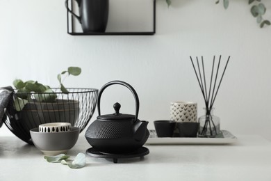 Photo of Stylish black teapot and beautiful green eucalyptus leaves on white table indoors