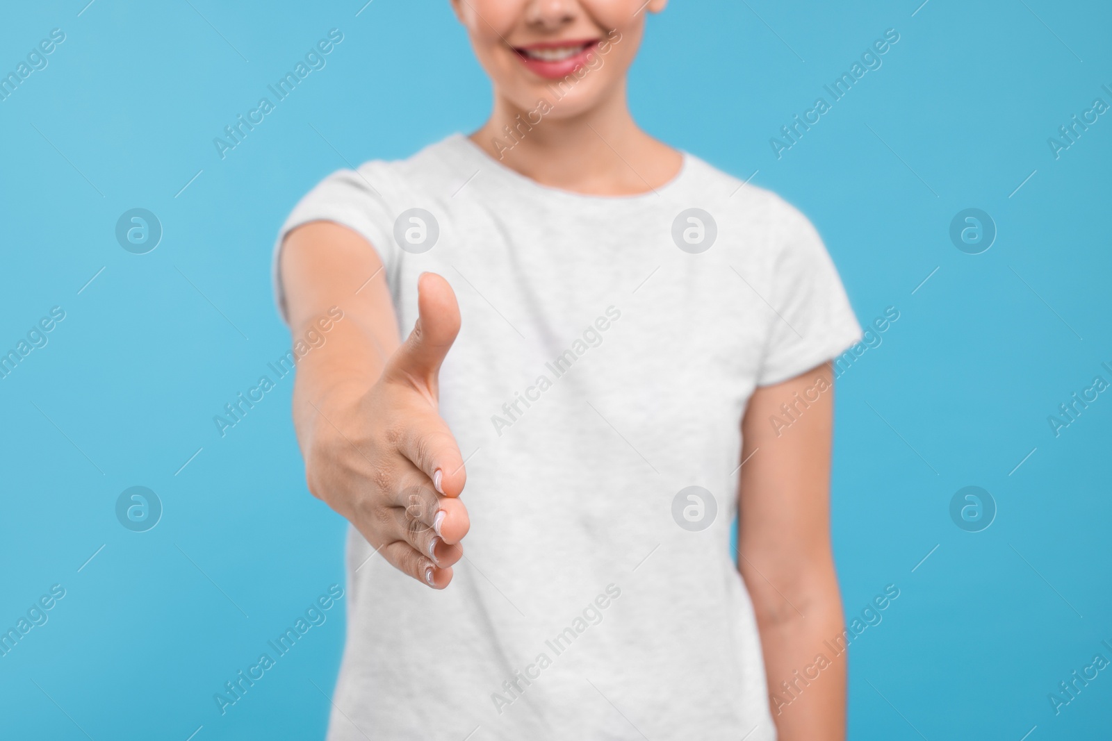 Photo of Woman welcoming and offering handshake on light blue background, closeup