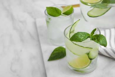Photo of Tasty fresh cucumber water with sliced lime and basil on white marble table. Space for text