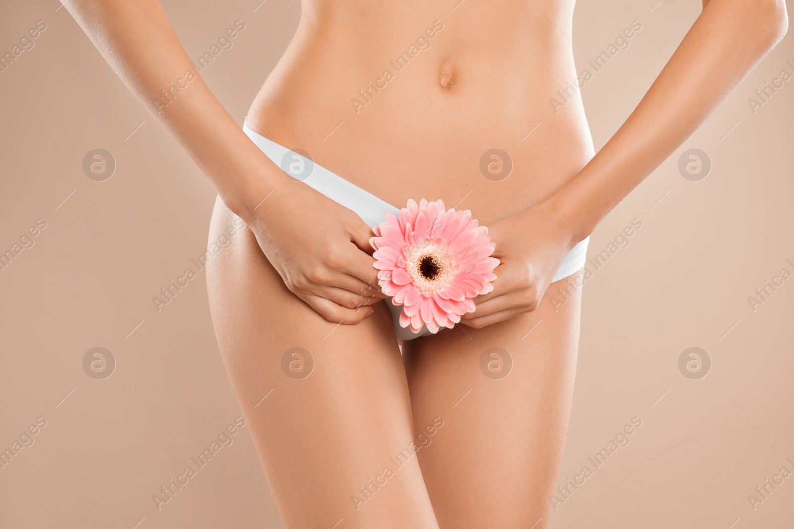 Photo of Woman with flower showing smooth skin after bikini epilation on beige background, closeup. Body care concept