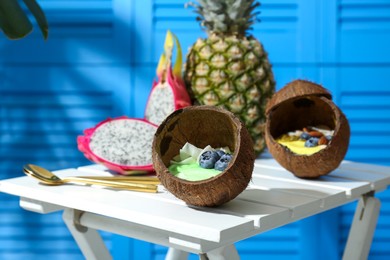Photo of Tasty smoothie bowl served in coconut shells on white wooden table