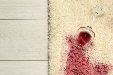 Photo of Overturned glass and spilled red wine on beige carpet, top view. Space for text