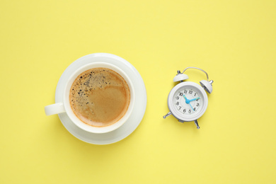 Photo of Cup of morning coffee and alarm clock on yellow background, flat lay