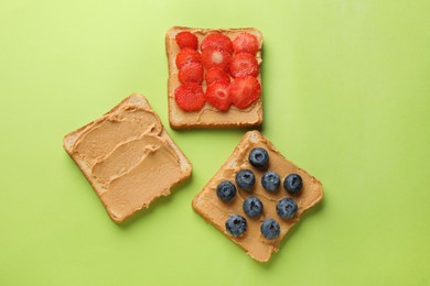 Photo of Tasty peanut butter sandwiches with fresh berries on light green background, flat lay