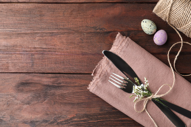 Cutlery set with quail eggs and space for text on wooden table, flat lay. Easter celebration