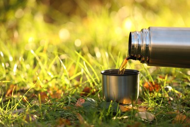 Pouring tea from thermos into cup lid on green grass outdoors, closeup. Space for text