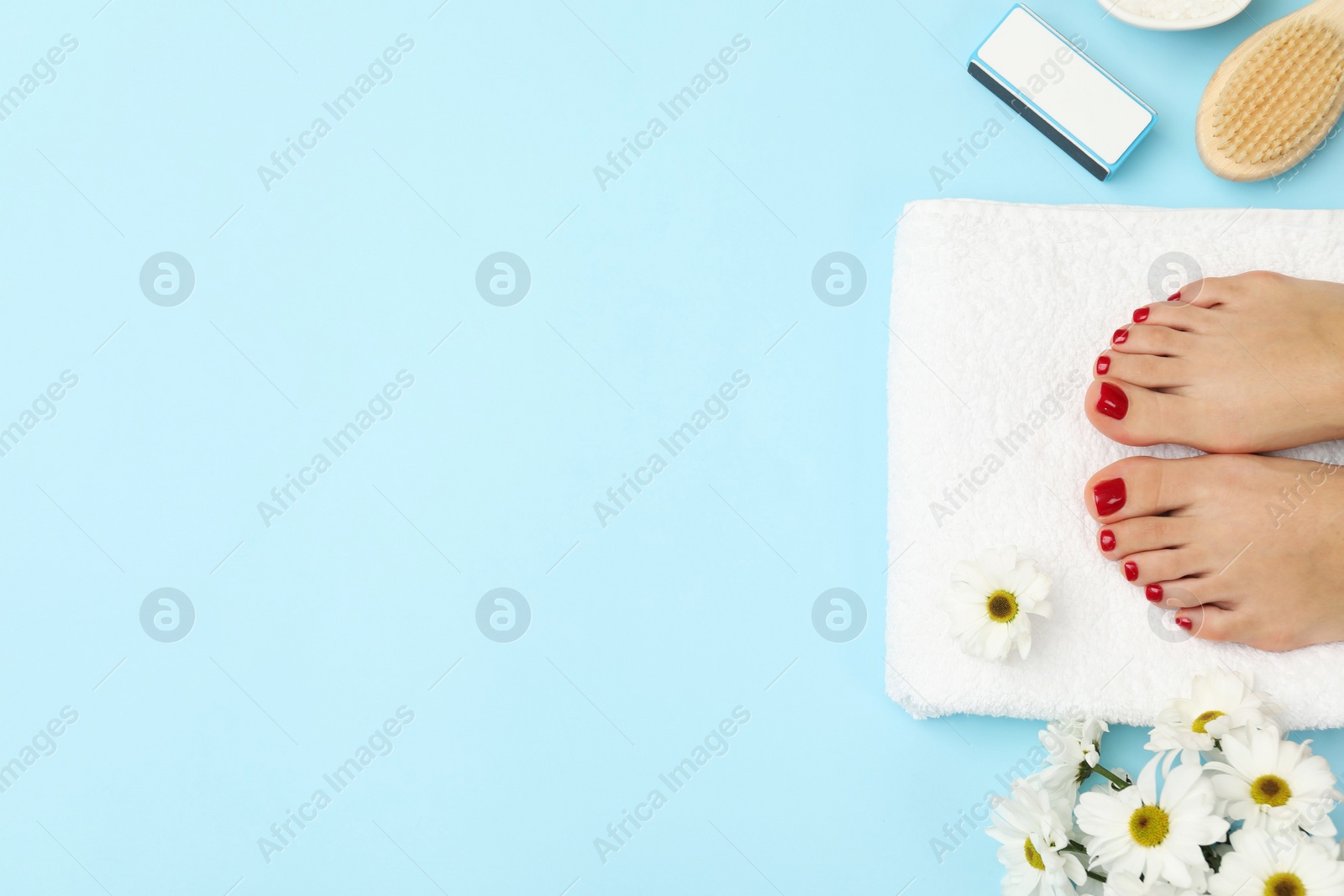 Photo of Woman with stylish red toenails after pedicure procedure and chamomile flowers on light blue background, top view. Space for text