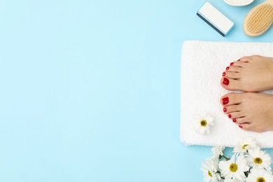 Woman with stylish red toenails after pedicure procedure and chamomile flowers on light blue background, top view. Space for text