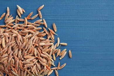 Photo of Pile of caraway seeds on blue wooden table, top view. Space for text
